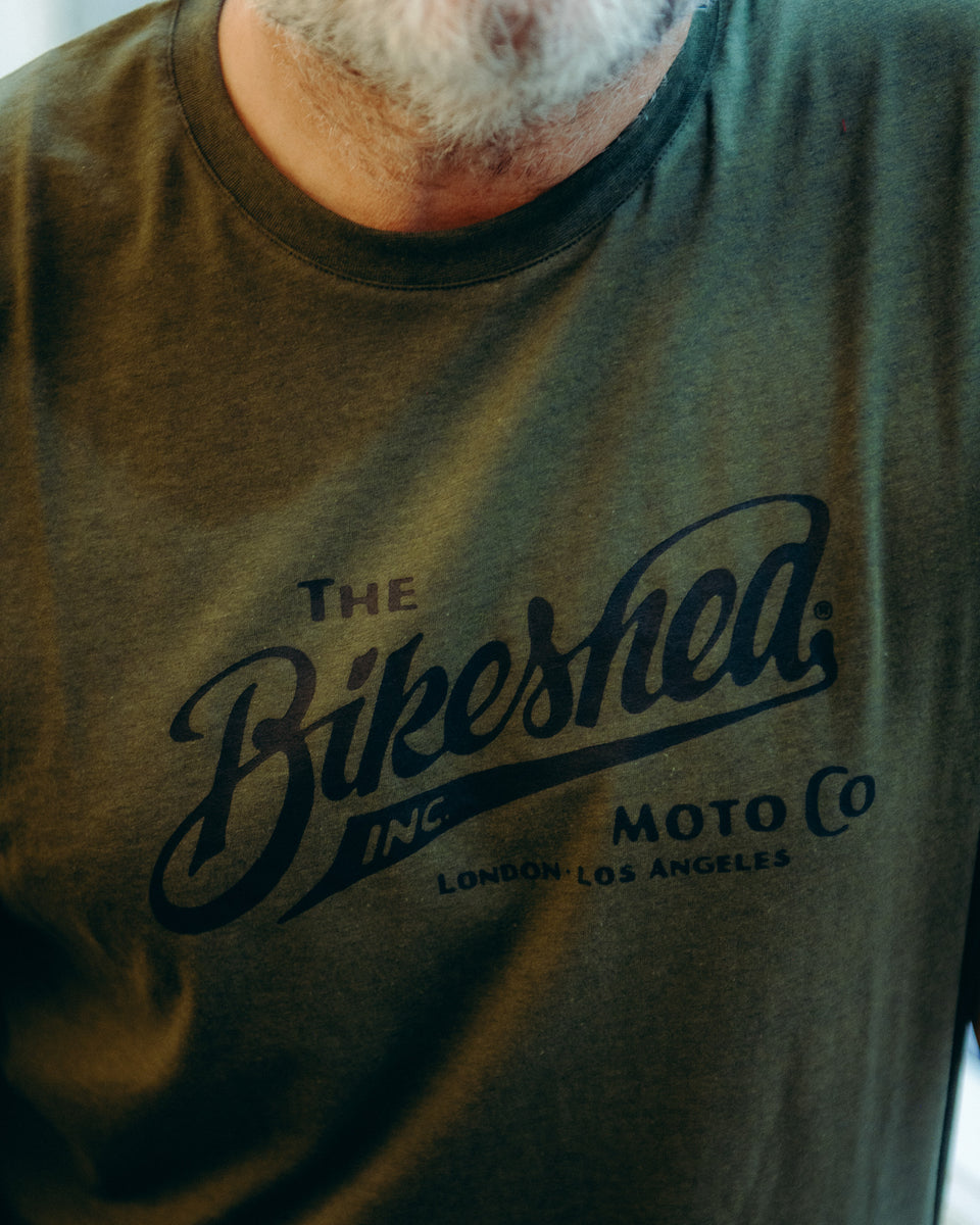 Model wearing Bike Shed Moto Co Inc T-Shirt Green in a white shop