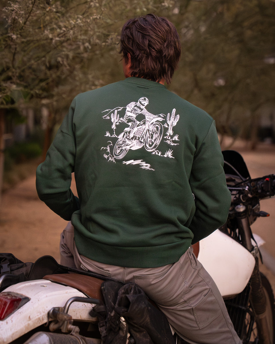 Model wearing Bike Shed Moto Desert Race Embroidered sweatshirt with a motorcycle in a dusty area
