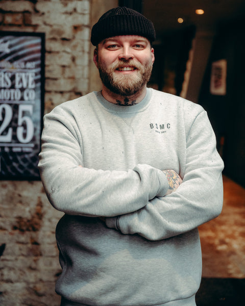 Model wearing Grey Bike Shed Moto Co ESTD Logo Sweatshirt on brick driveway