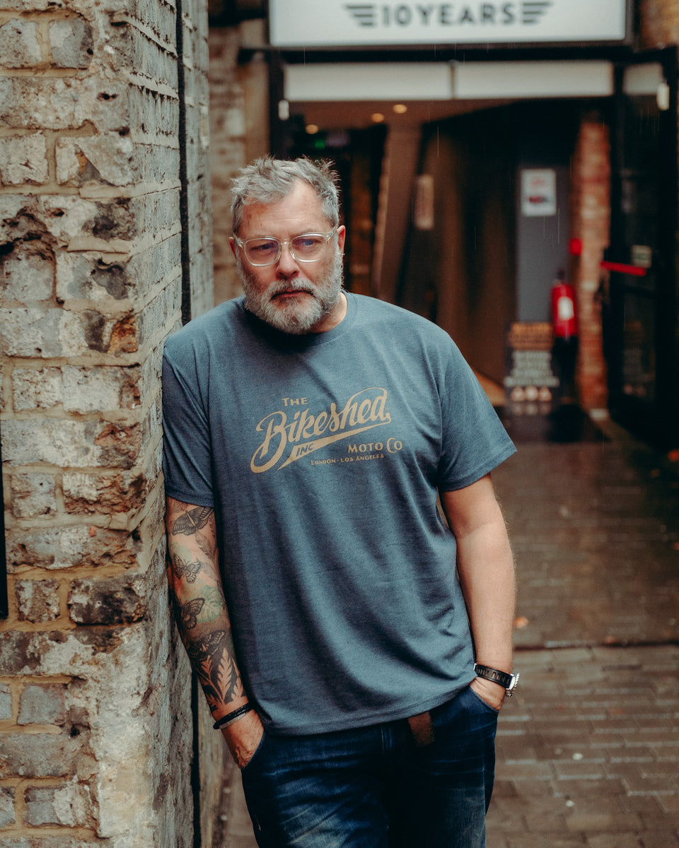 Model wearing Bike Shed Moto Co Inc T-Shirt Blue on brick driveway