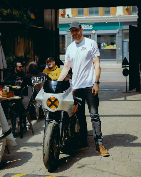 Model wearing Bike Shed Motorcycle Race T-Shirt White next to a custom motorcycle.