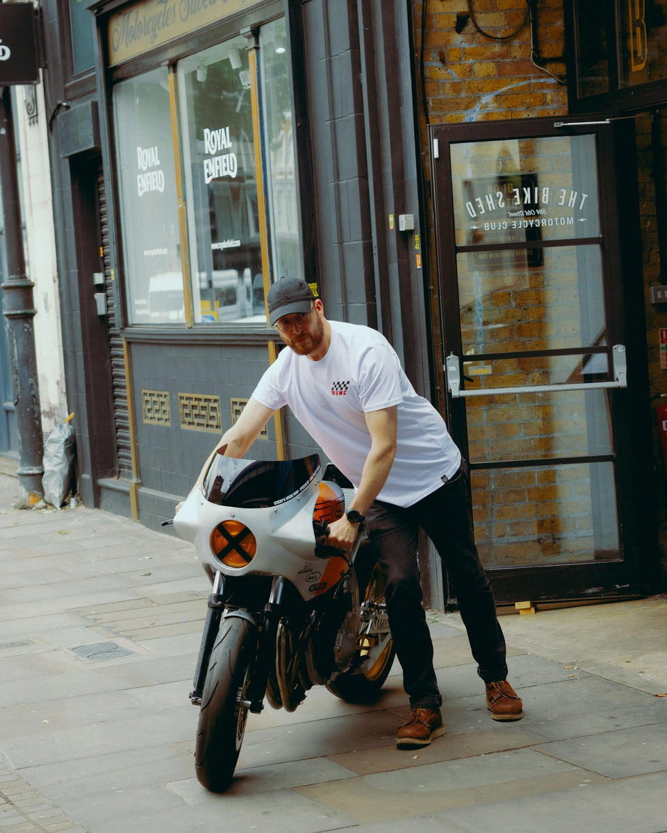Model wearing Bike Shed Motorcycle Race T-Shirt White next to a custom motorcycle.